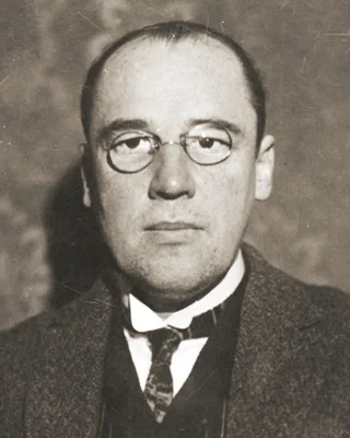 Wacław Sierpiński 1928: ein Mann mit hoher Stirn und runder Brille, in Anzug und Krawatte, ernst in die Kamera blickend.