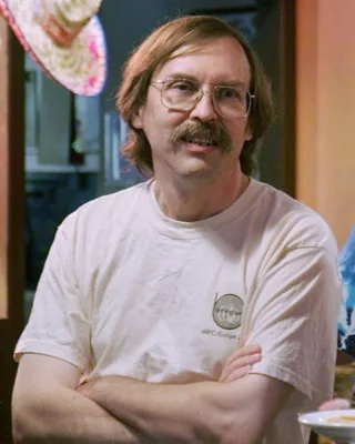 Larry Wall 2007: ein Mann mit langem rotblondem Haar, Brille und Schnurrbart in einem hellen T-Shirt, die Arme verschränkt.