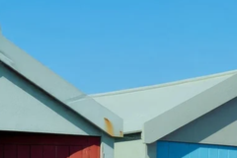 Eine Ecke der Strandhäuser: Himmel, zwei blasse Giebel, unten eine rote und eine hellblaue Tür.