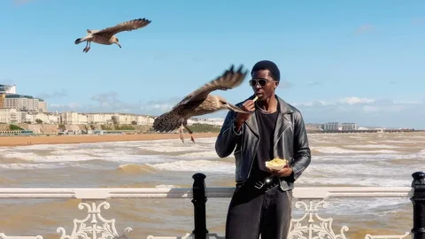 Ein Mann isst an der Strandpromenade Pommes, Möwen fliegen um ihn herum