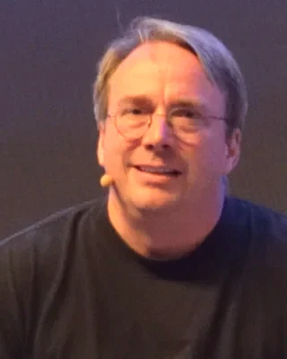 Linus Torvalds 2018 auf einer Konferenz: ein Mann mit Brille und kurzem Haar in einem schwarzen T-Shirt, lächelnd.