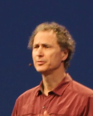 Michael Abrash 2015 auf einer Bühne: ein Mann mit lockigem Haar und Headset-Mikrofon in einem rotbraunen Hemd, im Sprechen.